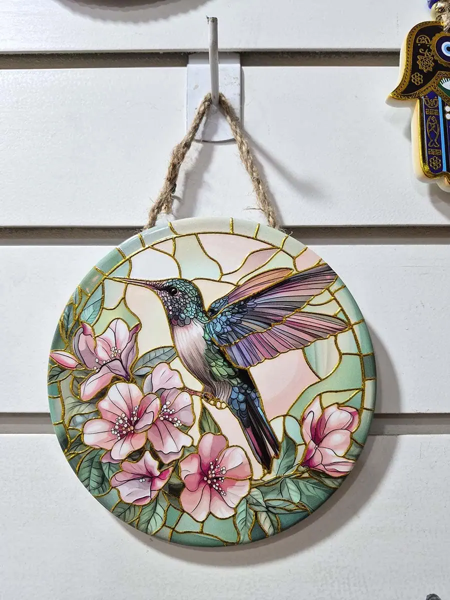 Colgante decorativo de pared de cerámica con un colibrí rodeado de flores rosadas y violetas