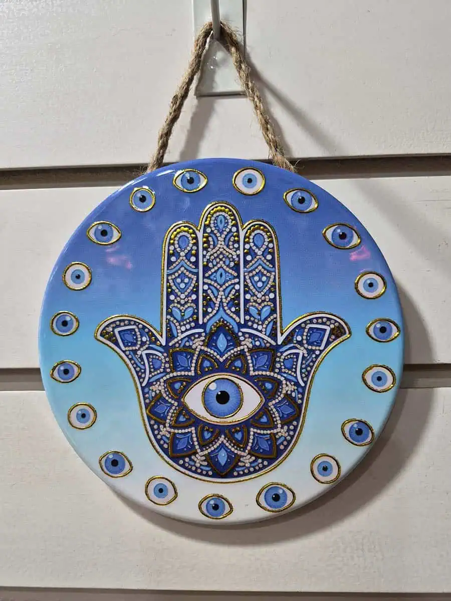 Colgante decorativo redondo de cerámica con Mano de Fátima y ojos turcos sobre fondo celeste