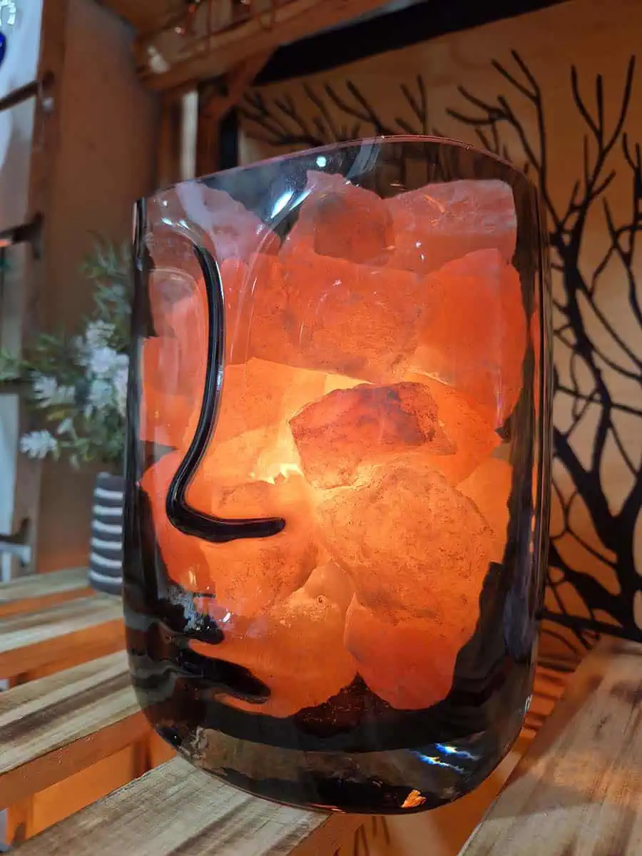 Lámpara de sal del Himalaya con piedras iluminadas dentro de un recipiente de vidrio con diseño de rostro